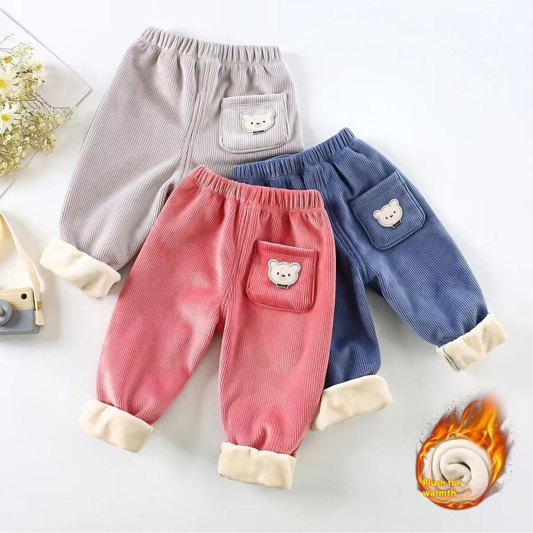 A cheerful parent shops online for baby clothes, smiling at a laptop, surrounded by soft, colorful outfits and cozy newborn essentials on a table.